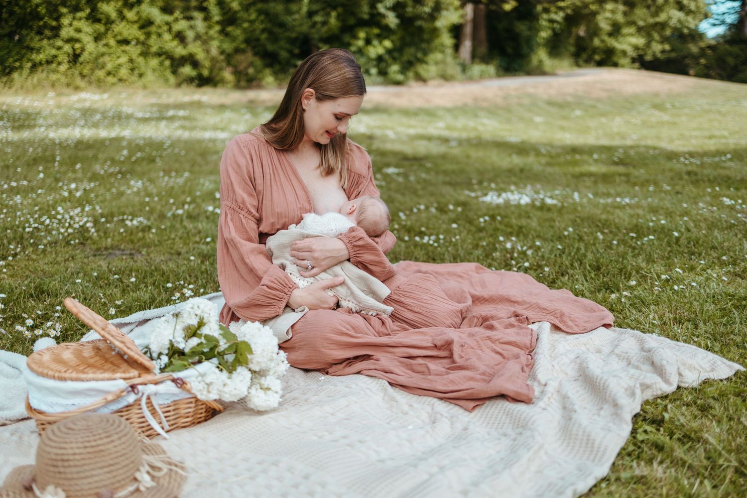 Someone in a pink dress sits on a picnic blanket in a sunny meadow with a picnic basket and white flowers nearby.