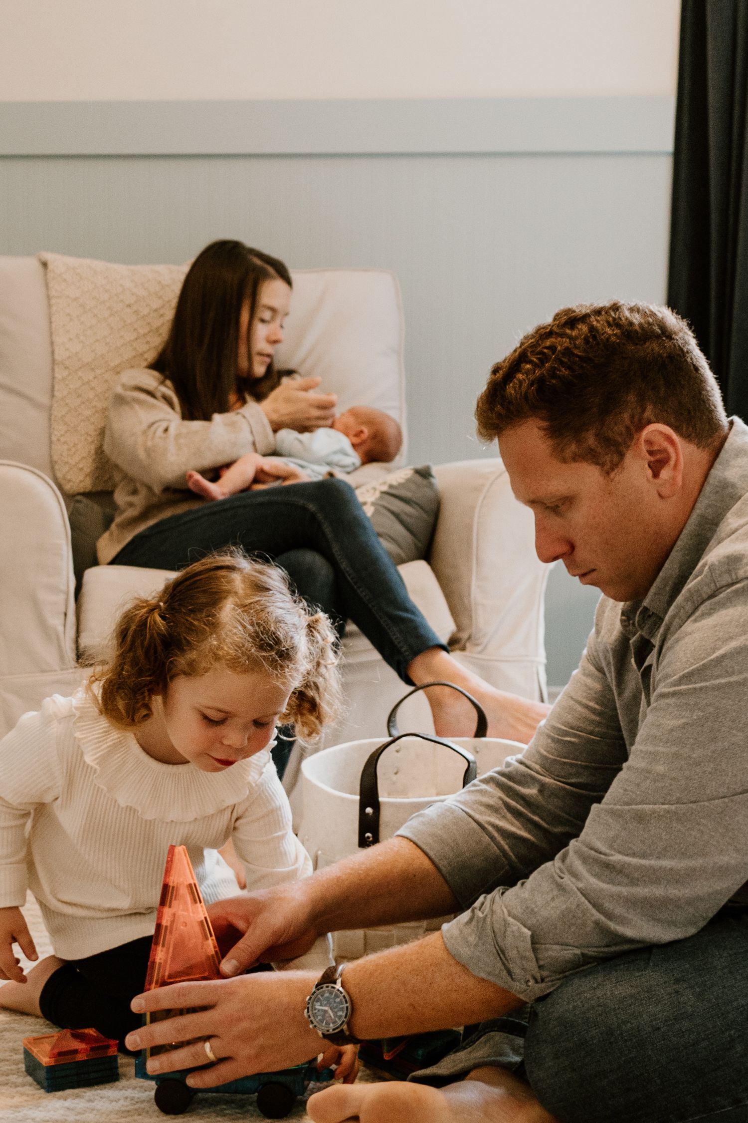 A family relaxes together in a living room as they play with toys on the floor.
