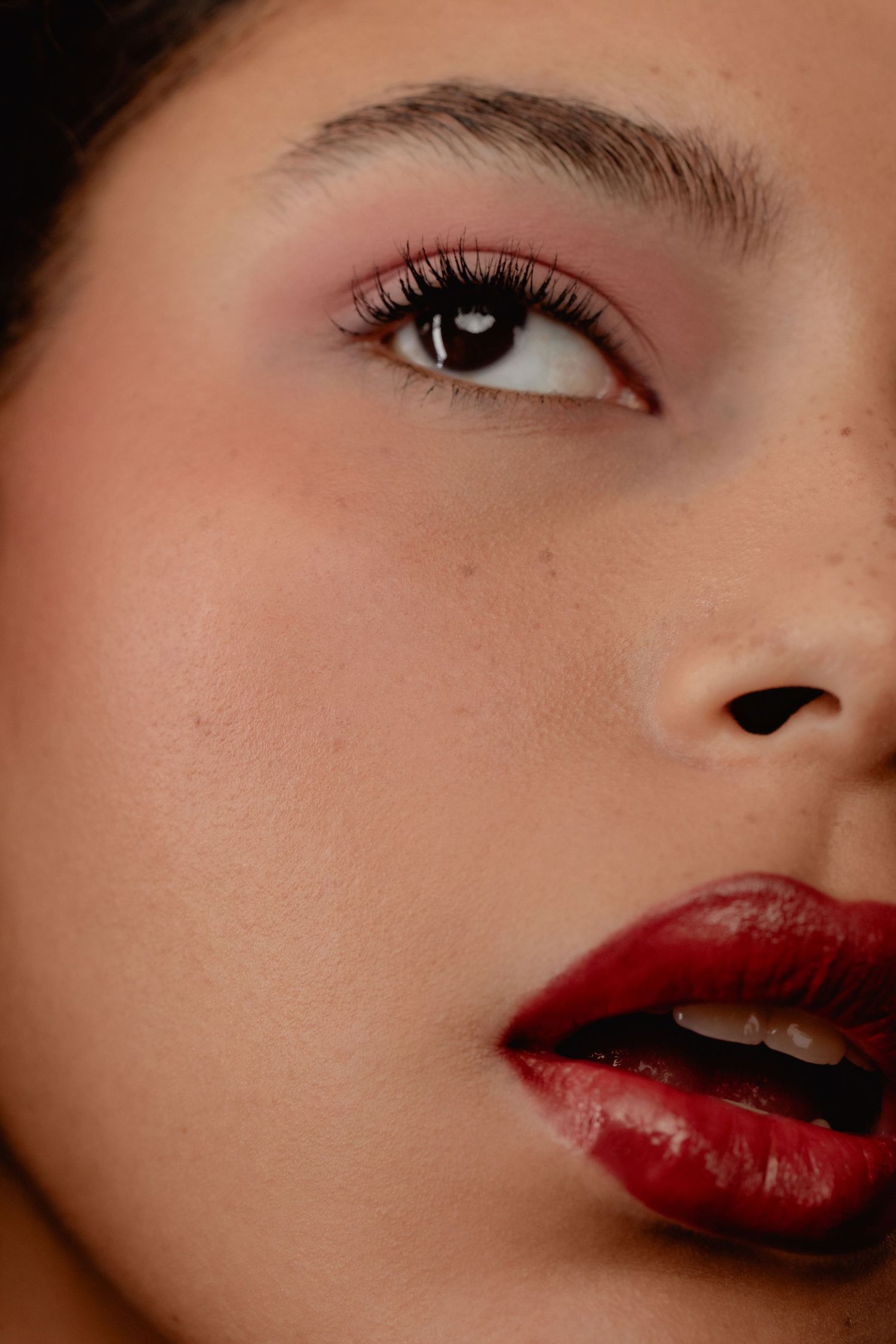 Close-up of a woman wearing bold red lipstick and pink eyeshadow with defined brows and long lashes.