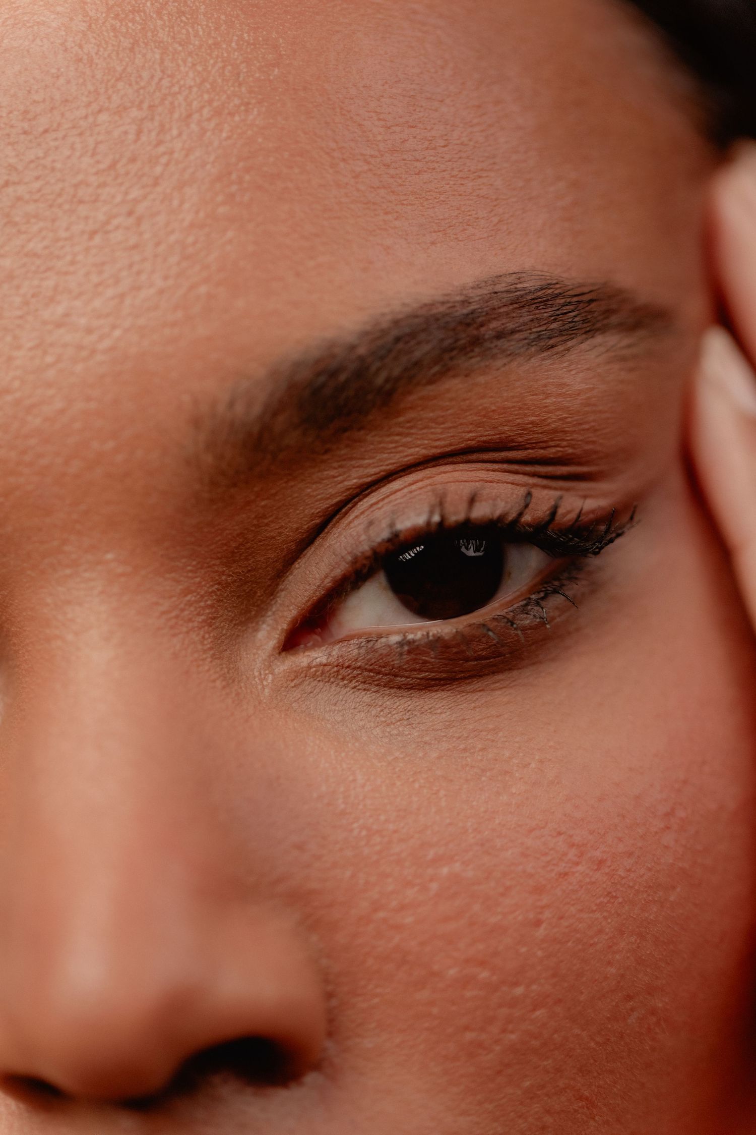Close-up of a woman's eye with subtle eye makeup, well-groomed brows, and glowing skin in warm tones.