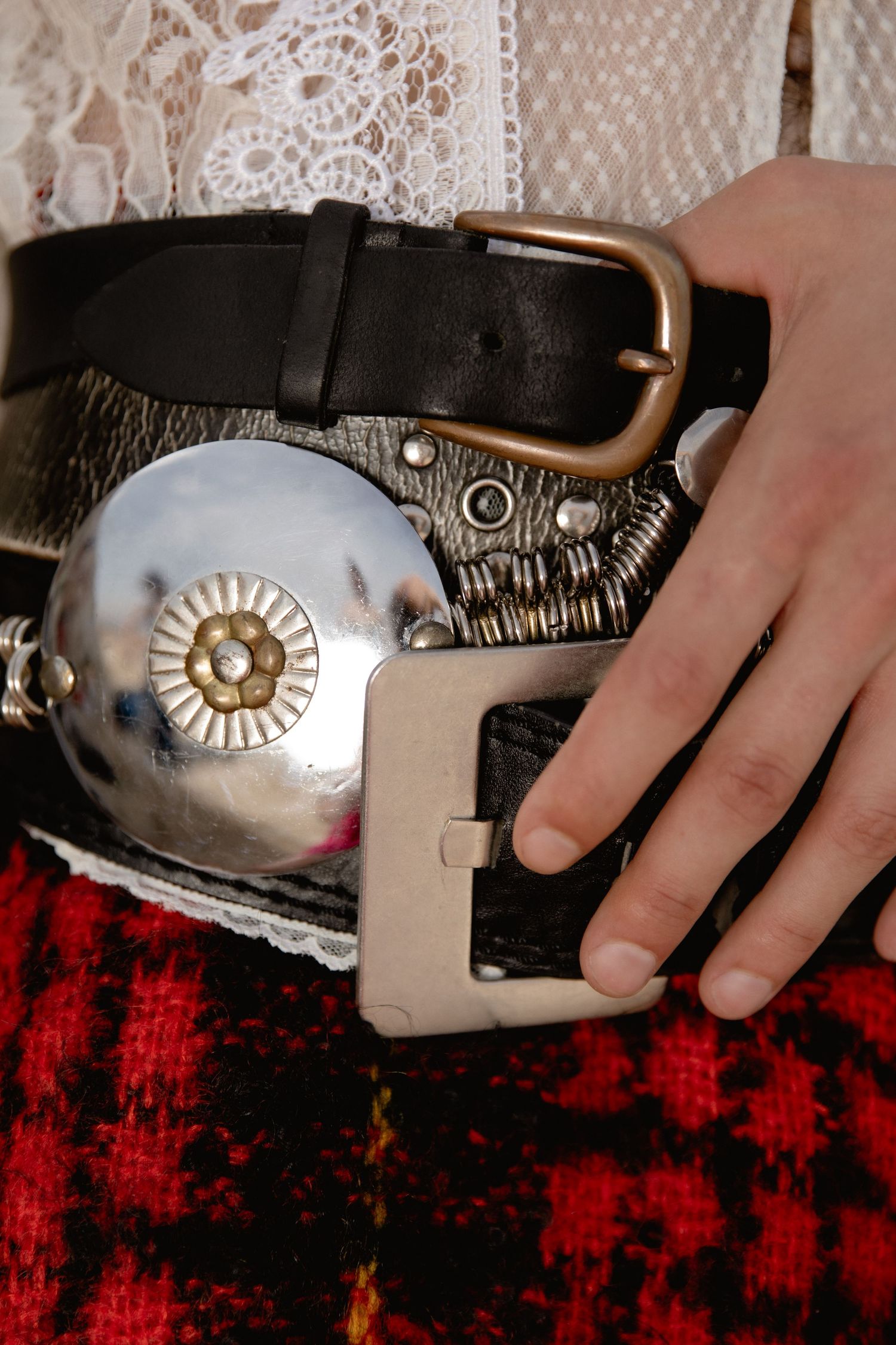A close-up view of hands holding a silver concho belt with decorative metal details against a red background.