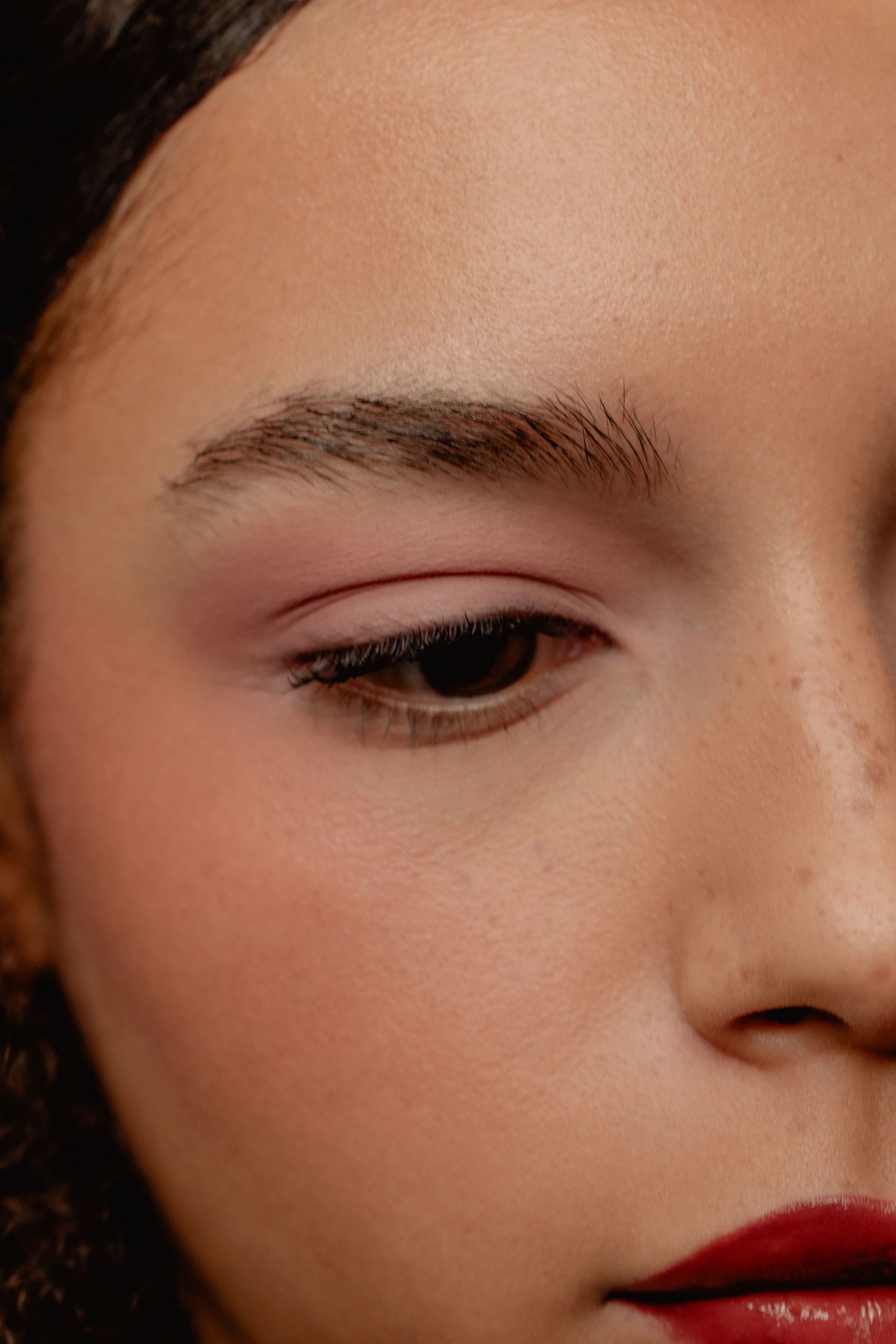 Close-up portrait of a young woman with bold brows, winged eyeliner, and red lipstick makeup look.