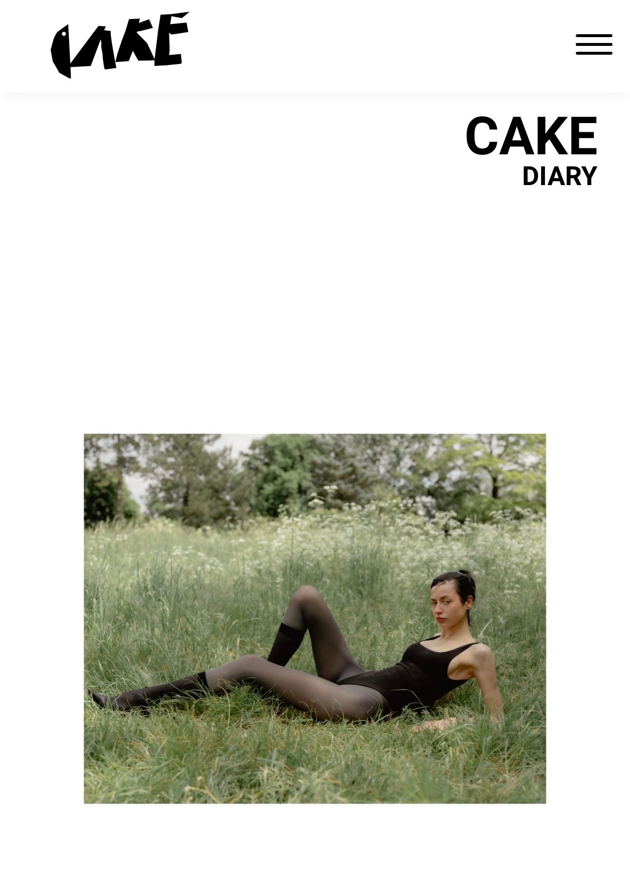 A woman in a black bodysuit and tights reclines gracefully in a lush green meadow filled with wildflowers.