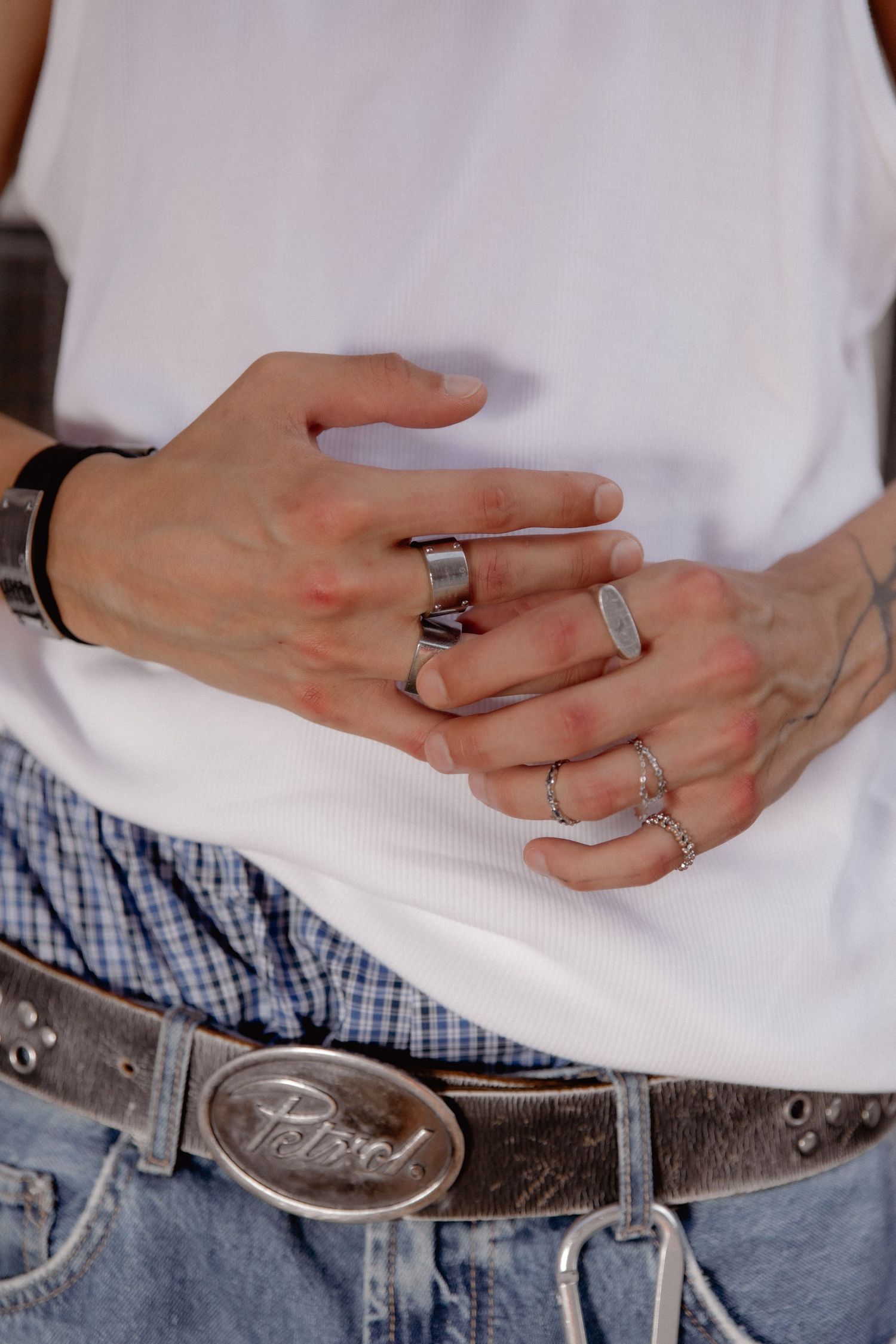 Close-up of hands wearing multiple silver rings against white shirt and jeans with a decorative leather belt.