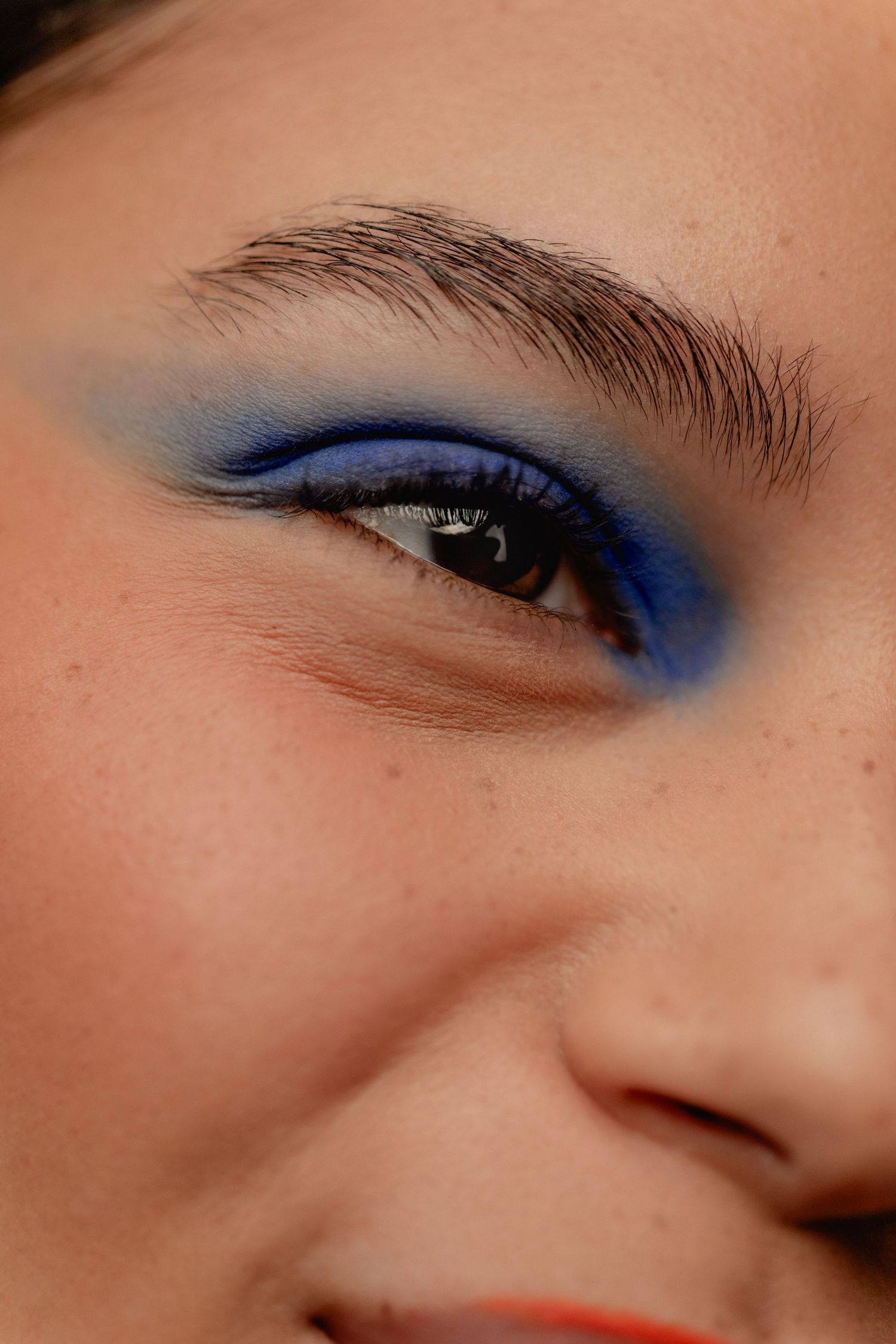 Close-up of a woman's eye with bold blue eyeshadow makeup and defined dark brows, showcasing a vibrant beauty look.