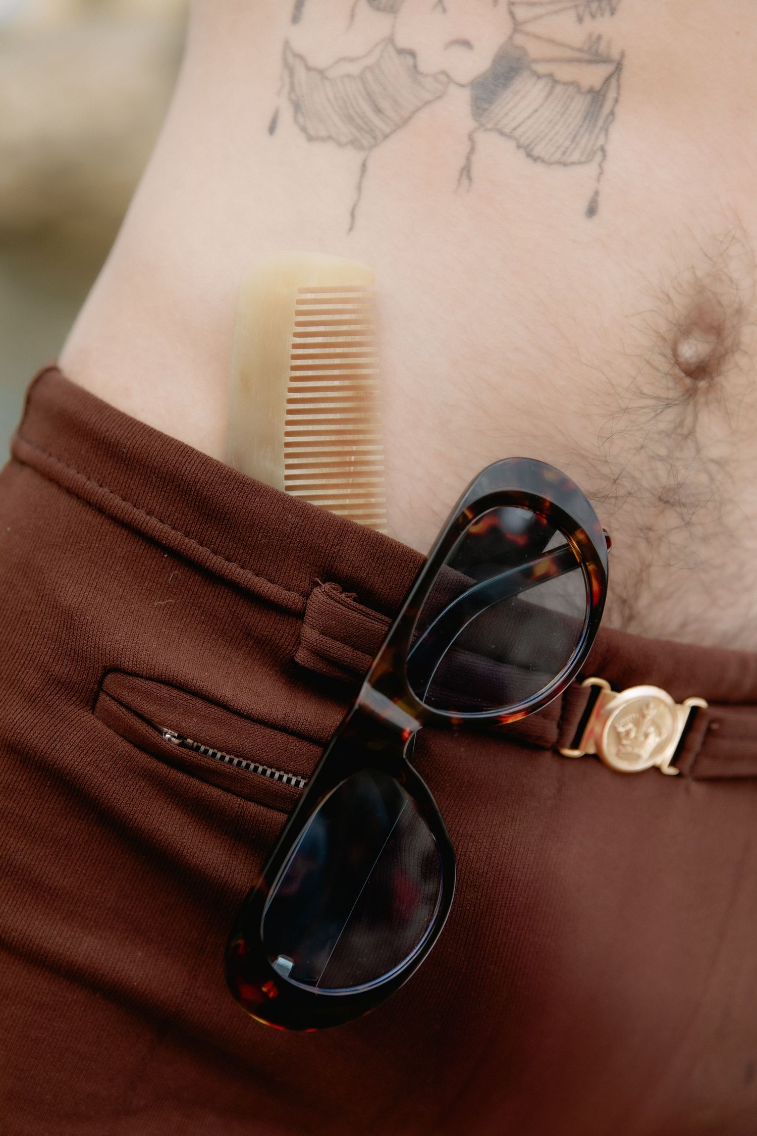 Tortoiseshell sunglasses and wooden comb rest on a brown leather surface with soft focus and warm lighting.