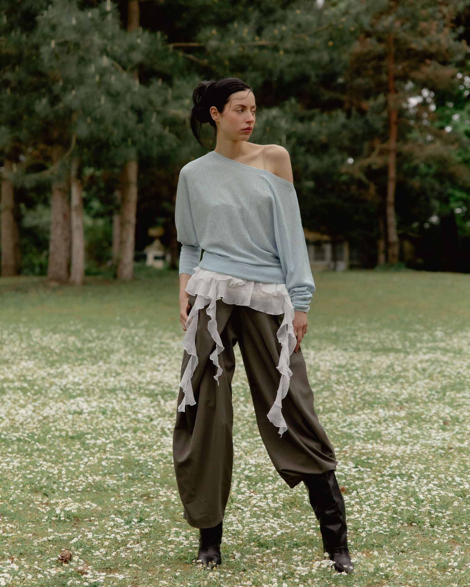 Woman in light blue off-shoulder top, ruffled hem, and olive wide-leg pants stands in a flower-filled meadow.