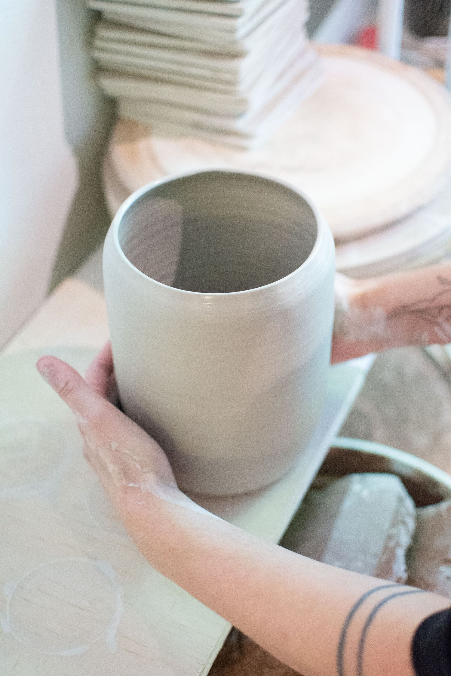 Close-up of hands holding a light gray ceramic vessel against a white background.