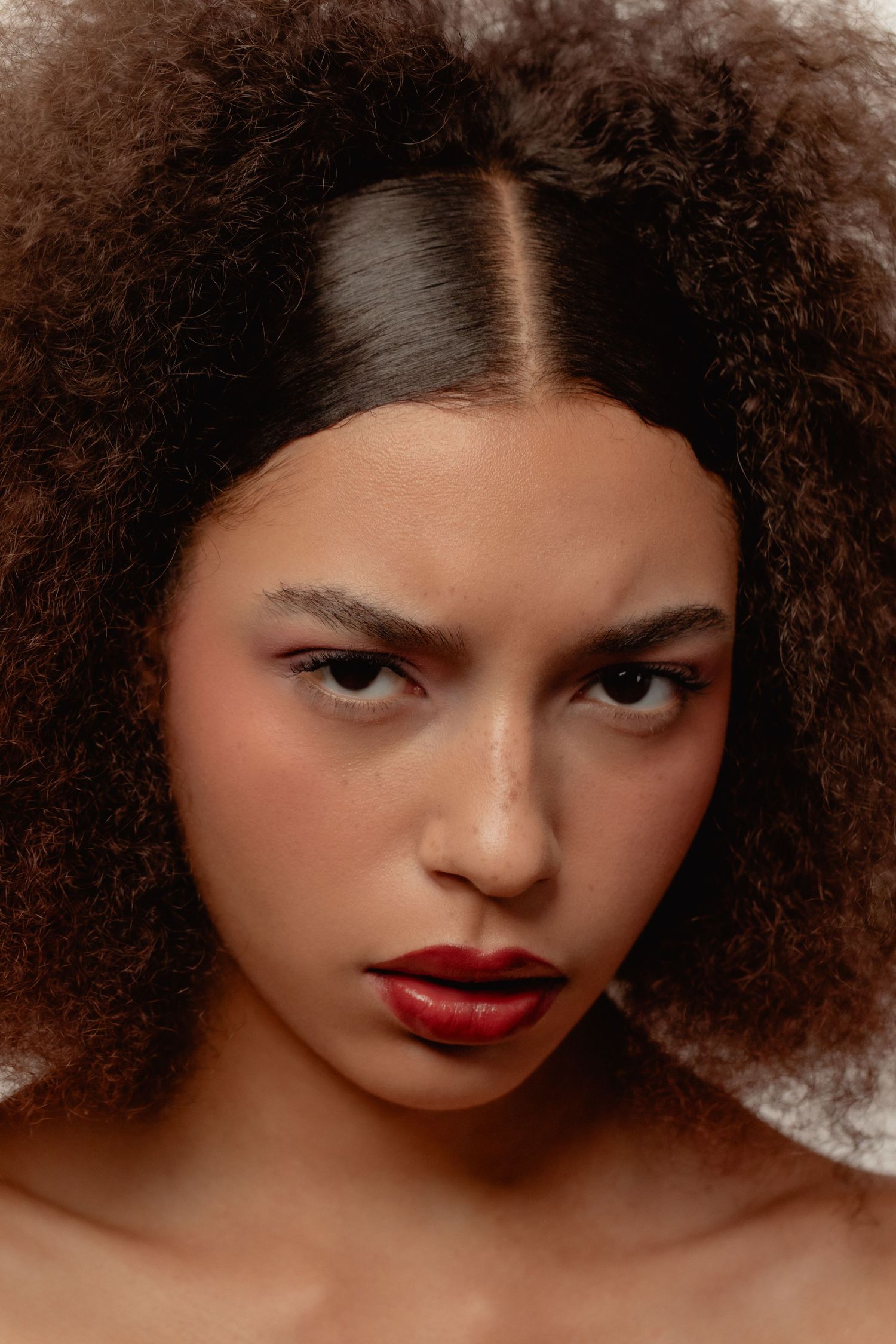Close-up portrait of a young woman with voluminous curly hair, red lips, and an intense expression.