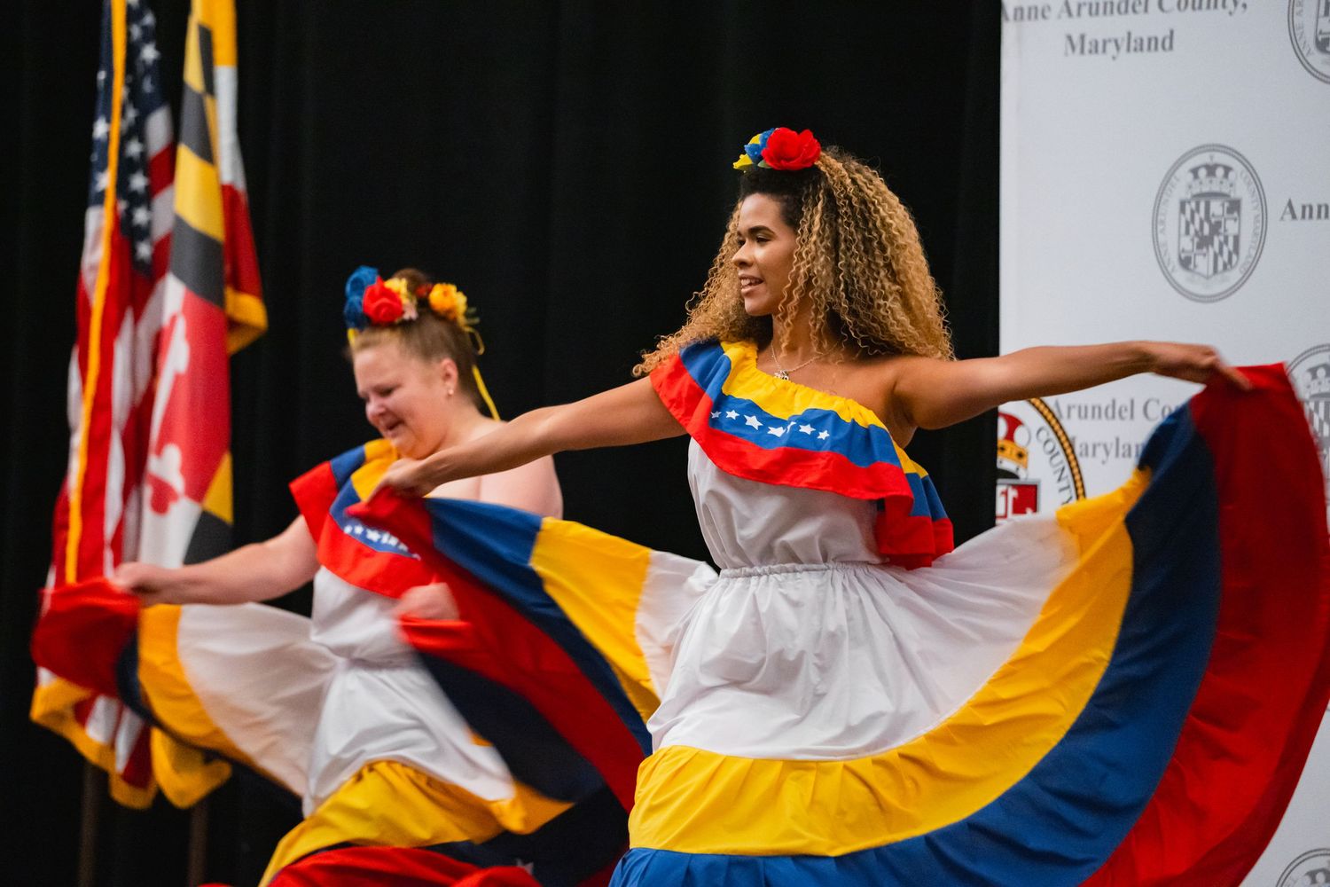 Two dancers perform in vibrant Venezuelan flag-colored dresses at an Anne Arundel County Maryland cultural event.
