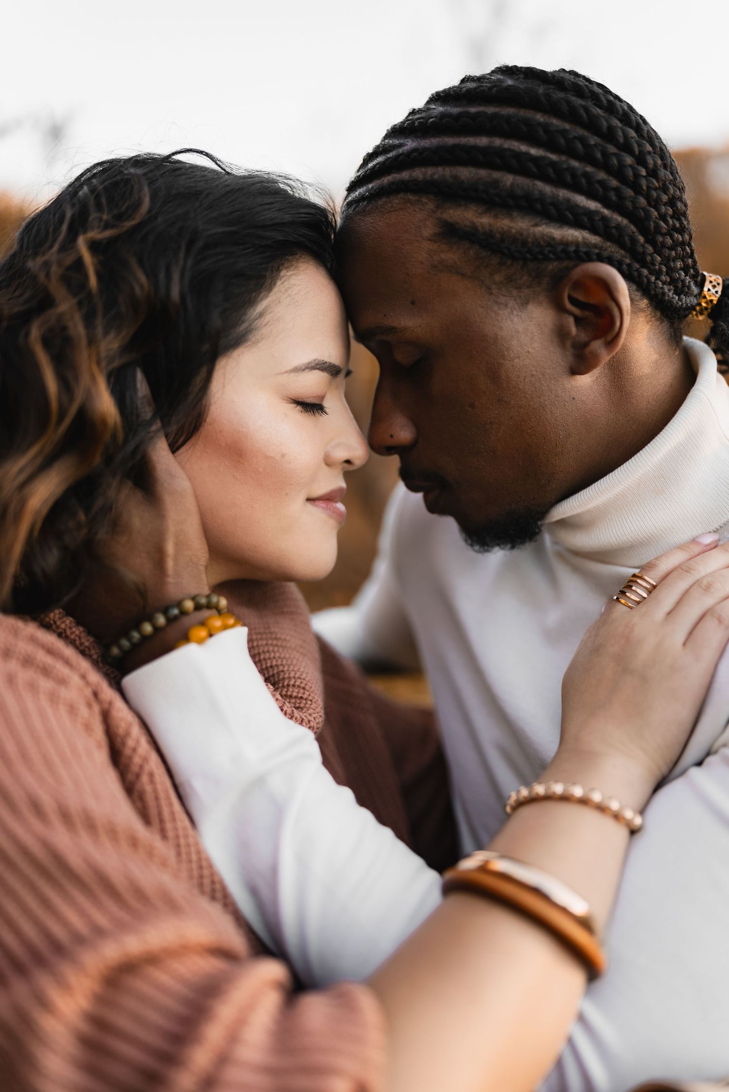 Interracial couple sharing a tender forehead-to-forehead moment with eyes closed in a warm outdoor setting.