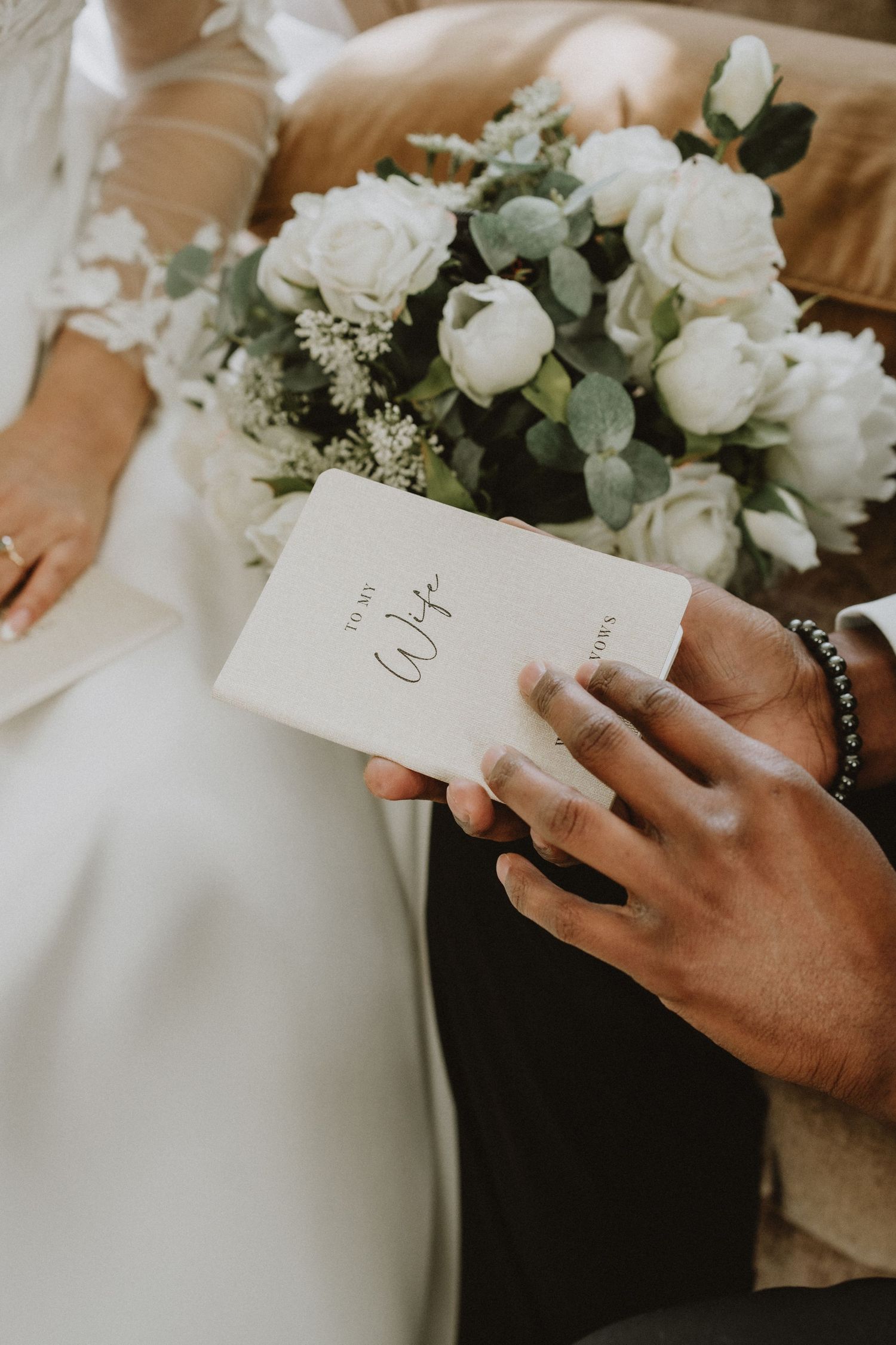 Groom holding a card addressed to his wife beside a white rose and eucalyptus bridal bouquet.