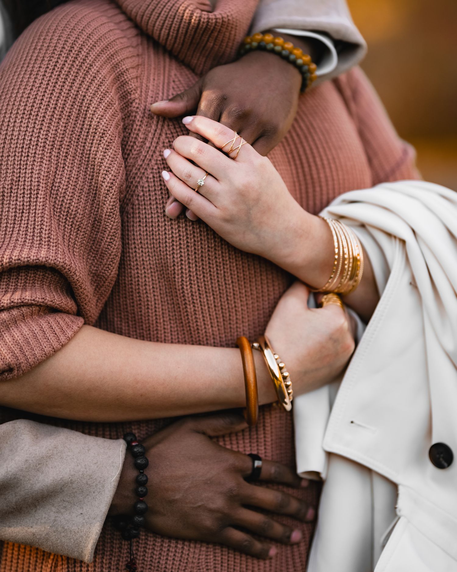 Two people sharing a warm embrace, showcasing gold bracelets and a diamond ring against cozy knit sweaters.