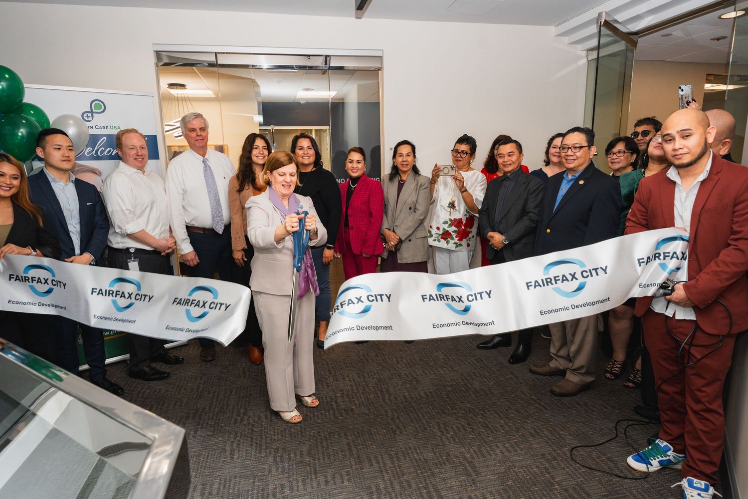 Group of people at a Fairfax City ribbon cutting ceremony celebrating a grand opening indoors.