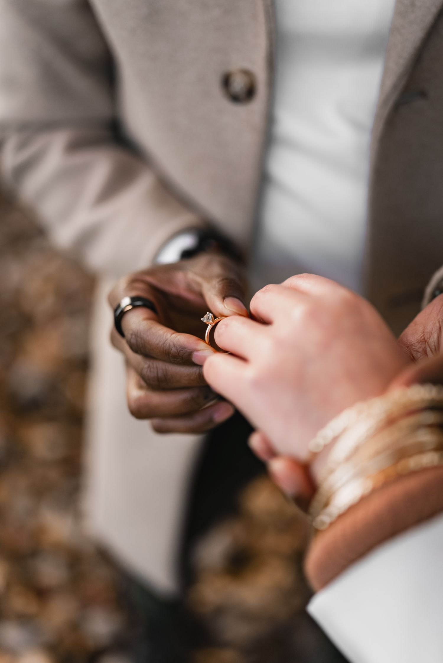 Close-up of a man placing a gold diamond engagement ring on a womans finger during a proposal.