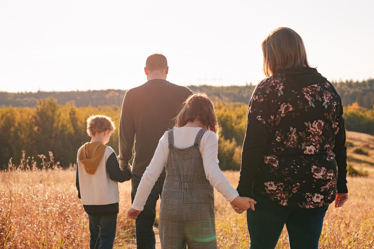 A family walking together through a golden autumn field at sunset with trees on the horizon.