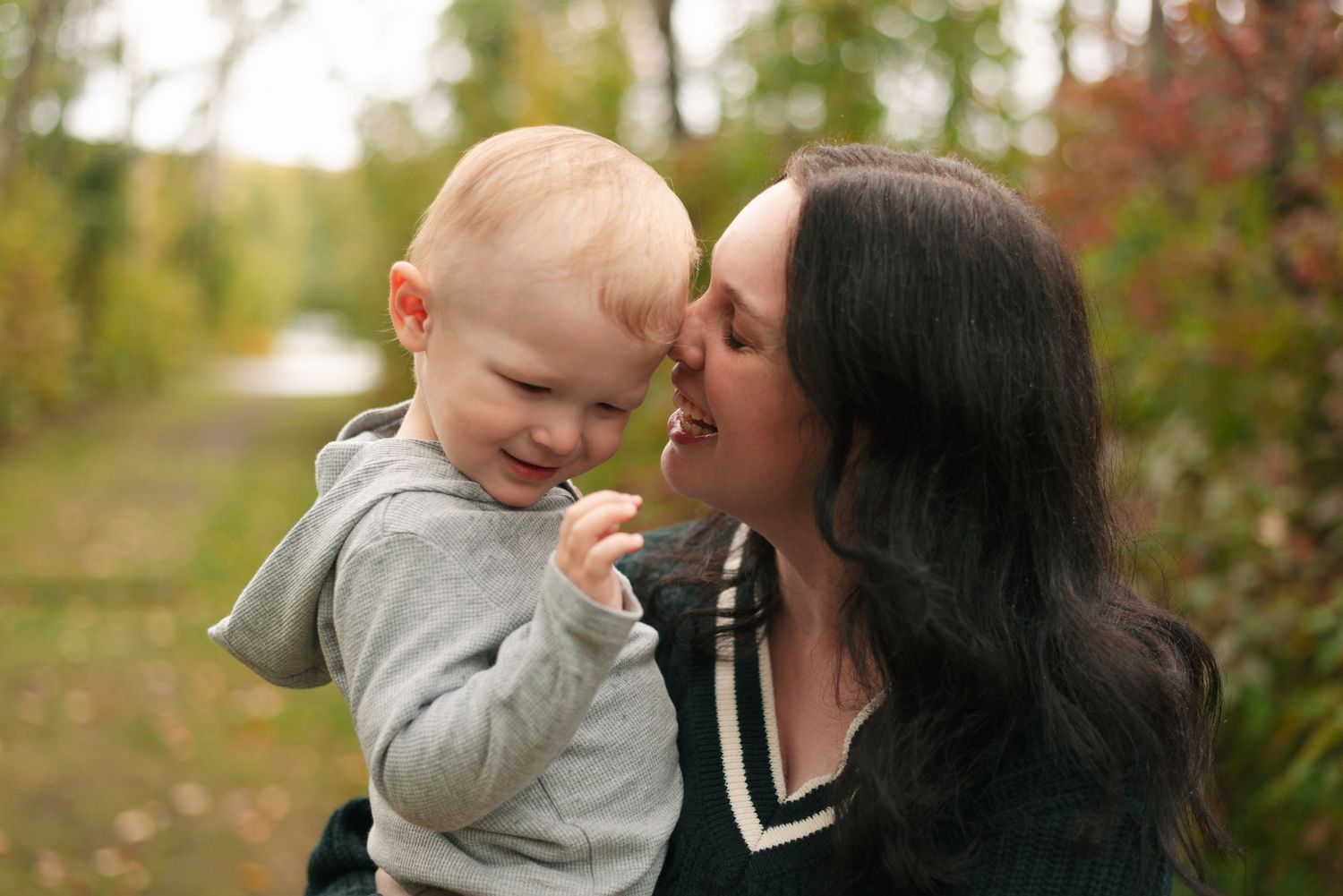 A tender outdoor autumn moment between parent and child in a sun-dappled, leaf-strewn setting.