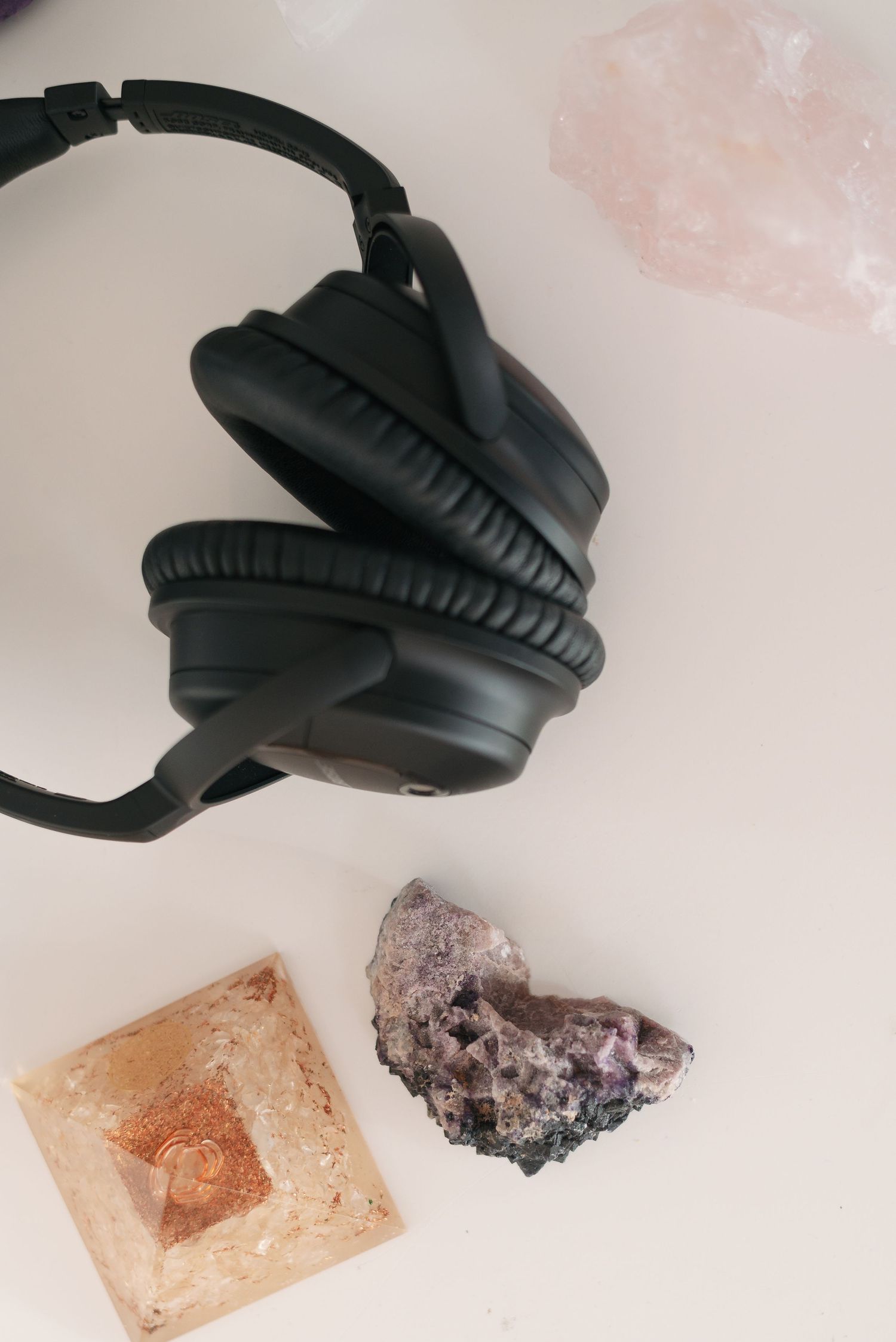 Black wireless headphones resting on pink and brown mineral stones against a light background.