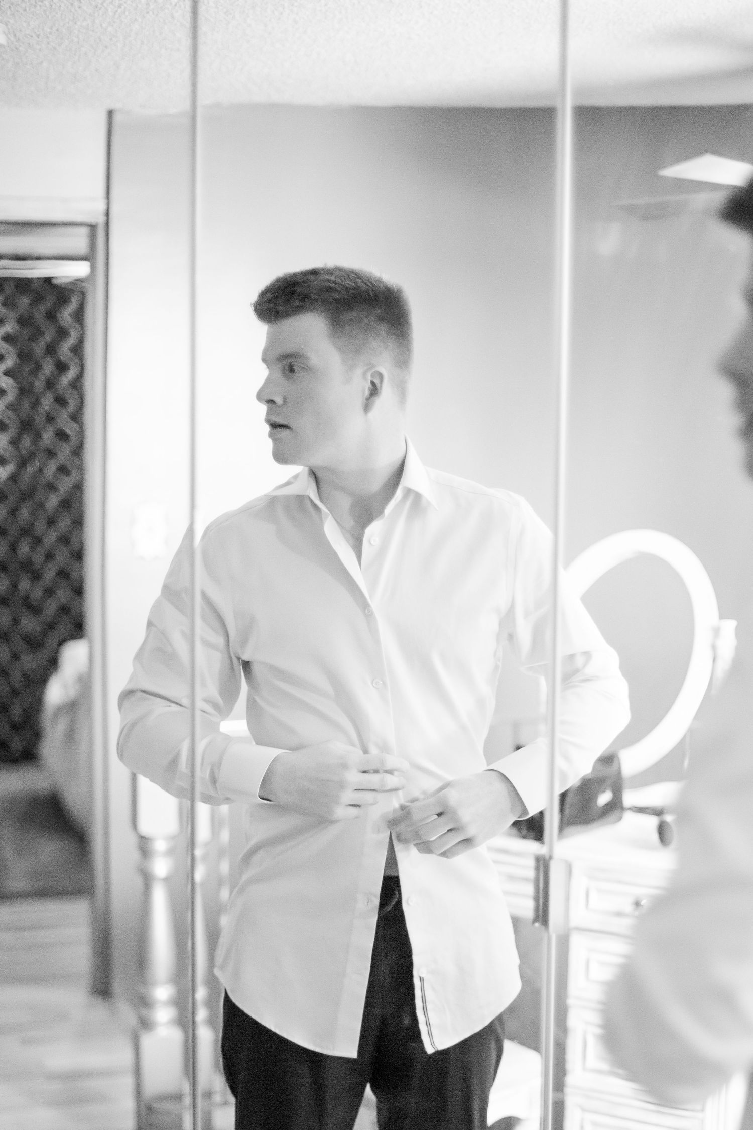 Black and white photo of someone in a crisp white button-down shirt looking to the side in a room with mirrors.