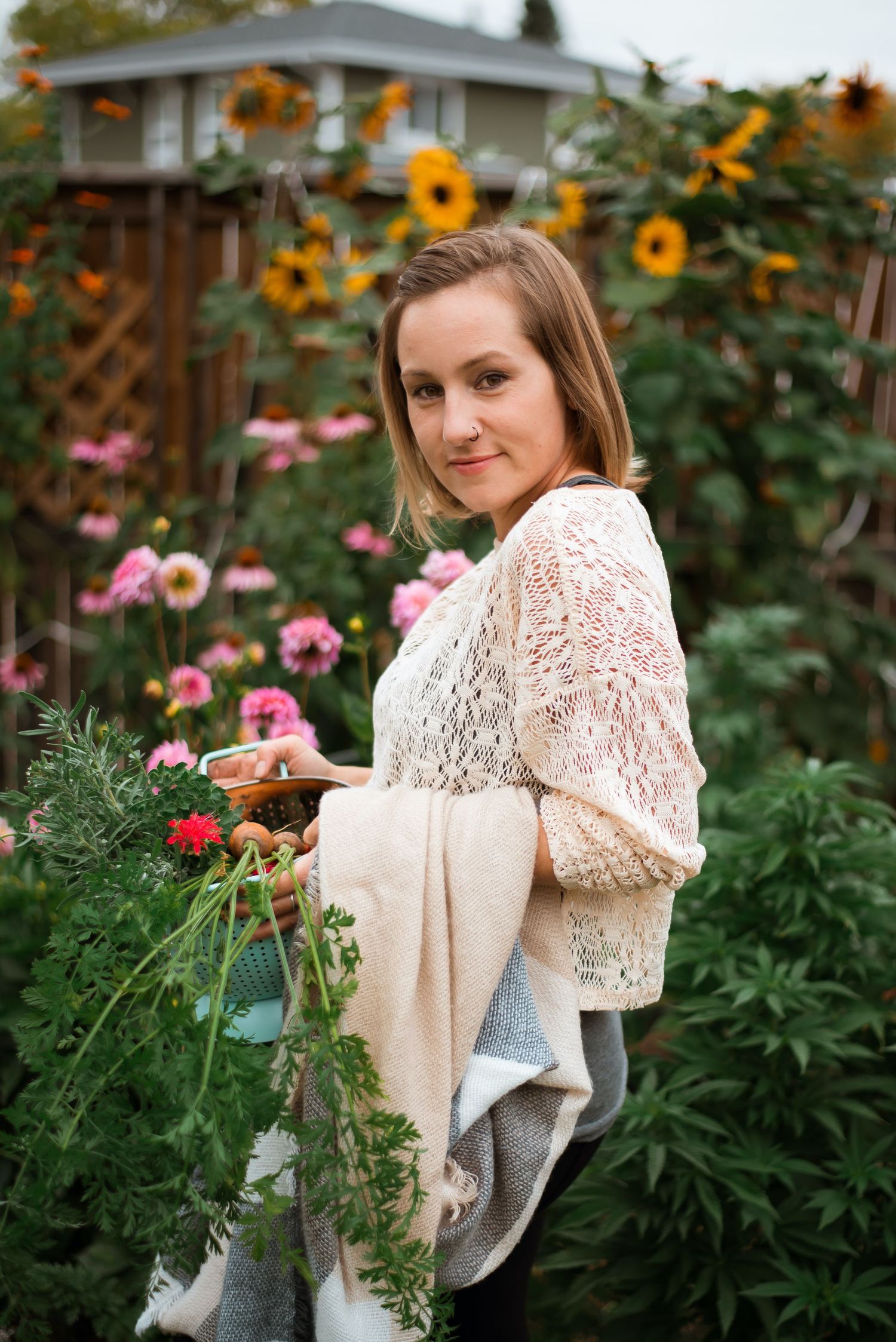 Woman in lace top holding fresh flowers in a vibrant garden with sunflowers and pink blooms.