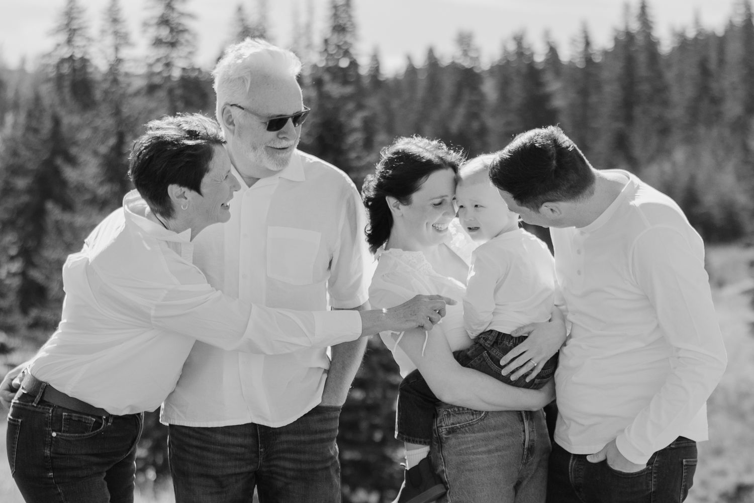A joyful black and white outdoor photo showing a group of people in white shirts laughing together against a forest backdrop.