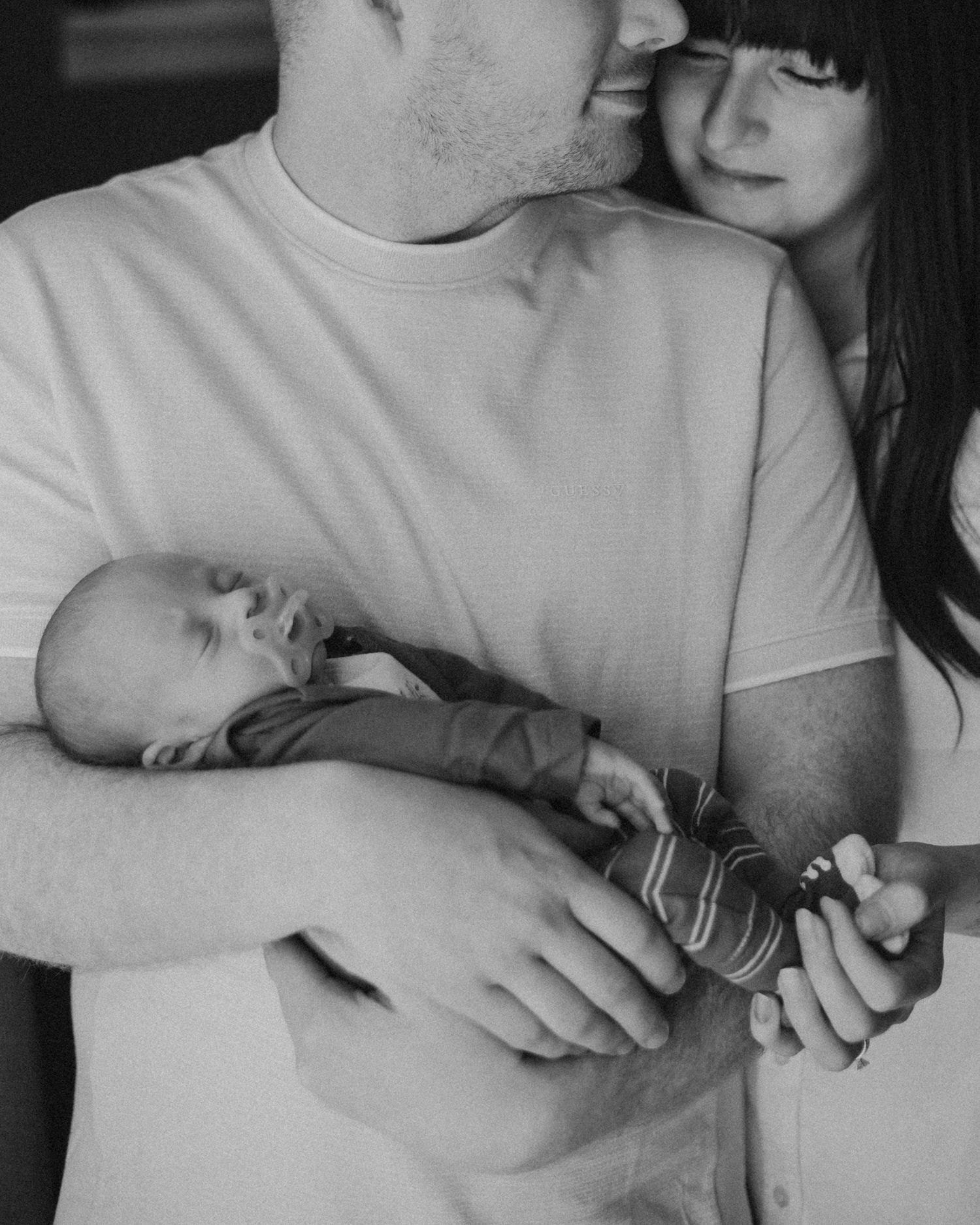 A tender black and white family moment showing parents holding their sleeping newborn baby in an intimate embrace.