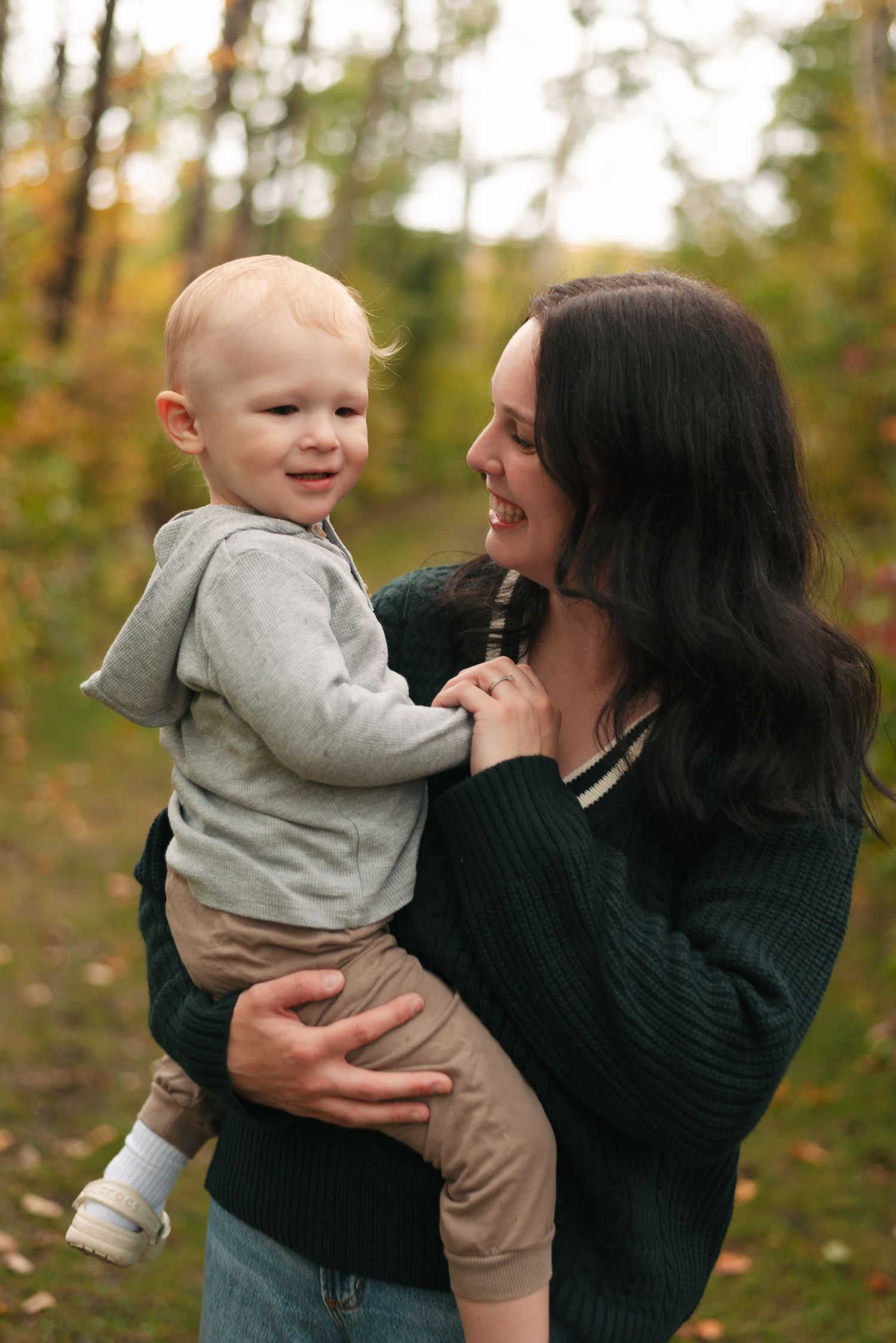 A tender autumn moment captured outdoors showing joyful interaction against a backdrop of fall foliage.