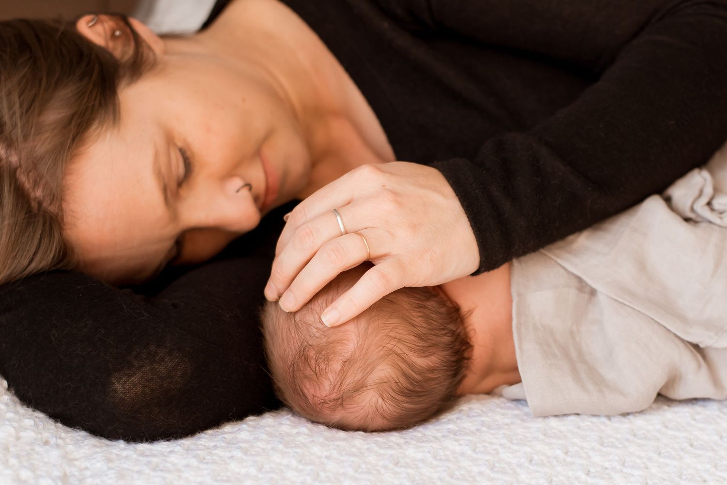 A parent and newborn baby share a tender bonding moment while resting together on white fabric.