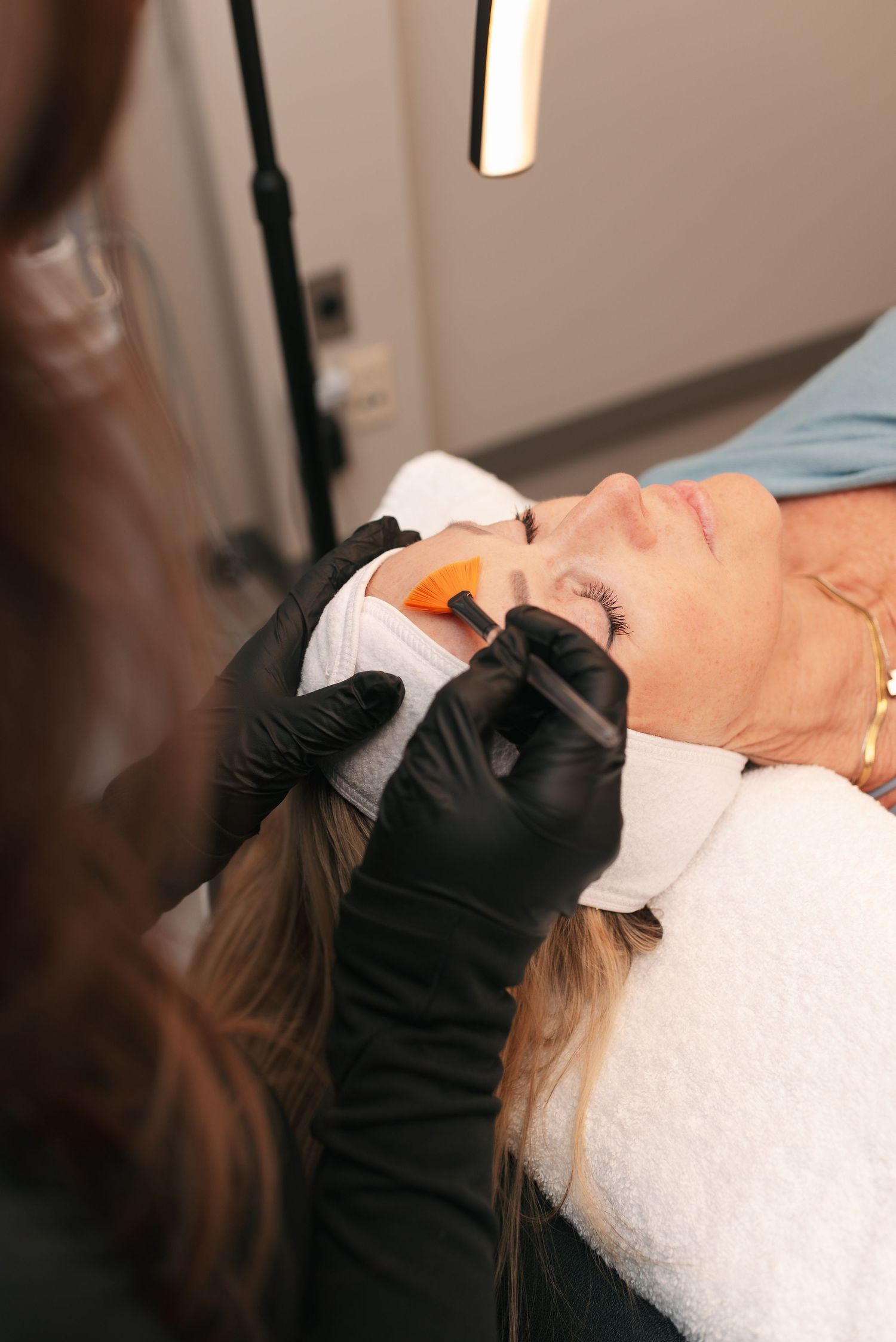Hands wearing black gloves perform a professional facial treatment with white towel in a spa setting.