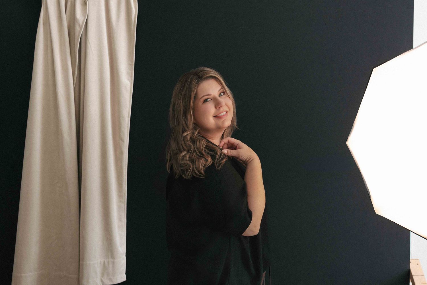 Woman in black outfit posing gracefully in a photography studio with a softbox light and white backdrop.
