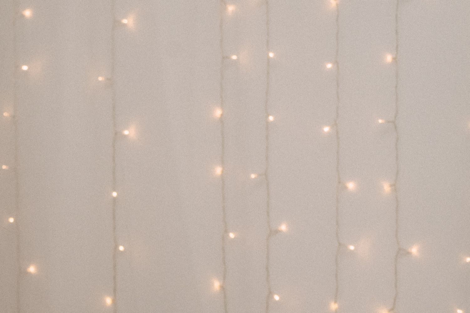 Glowing warm white LED string lights create a delicate curtain effect against a light gray background.