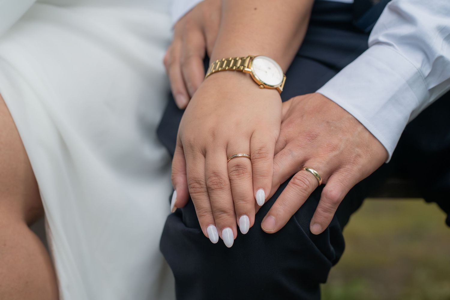 Close-up of newlyweds hands showing wedding rings, bride wearing gold watch and white manicure.