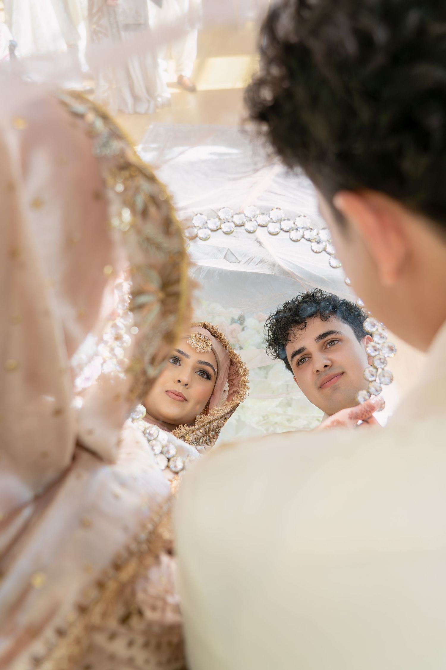Bride and groom in traditional South Asian wedding attire share an intimate moment, viewed from a unique low angle perspective.