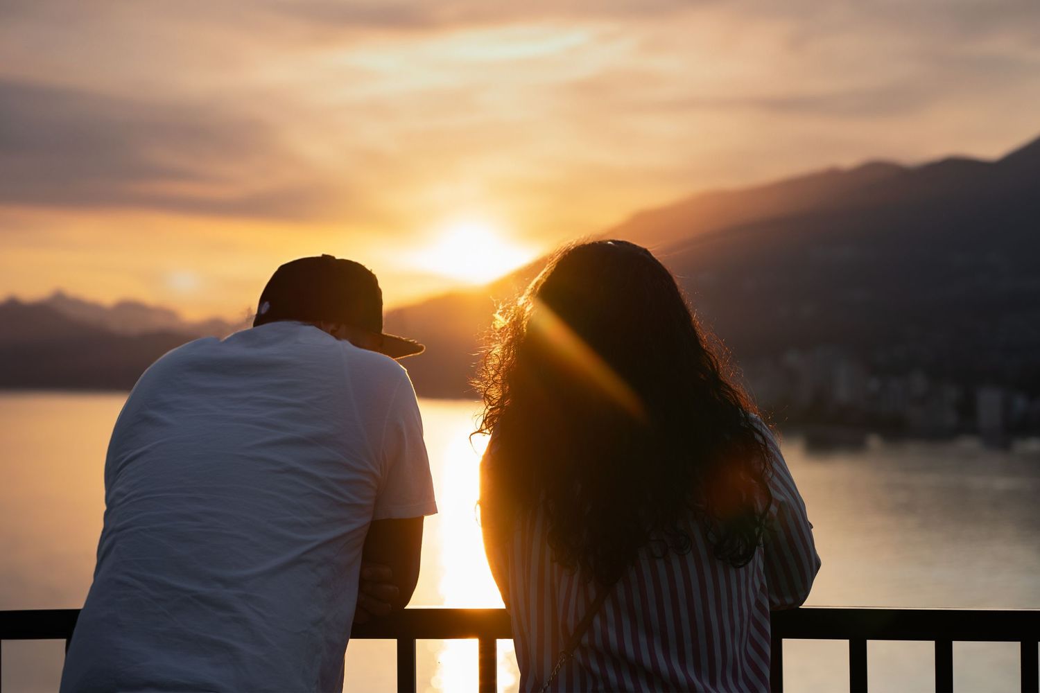 Romantic silhouettes against dramatic orange sunset sky over coastal mountains.