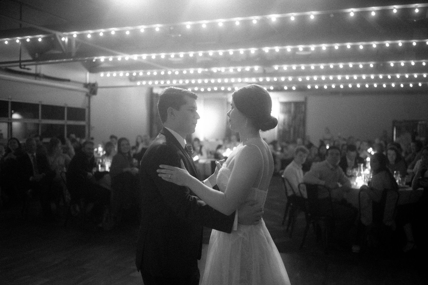 Couple shares their first dance under romantic string lights at an outdoor evening wedding reception.