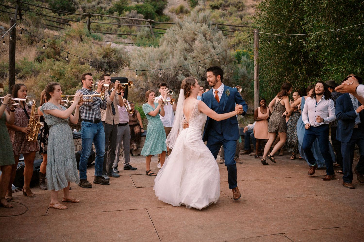 Wedding guests watch and photograph a couple dancing at an outdoor desert venue.