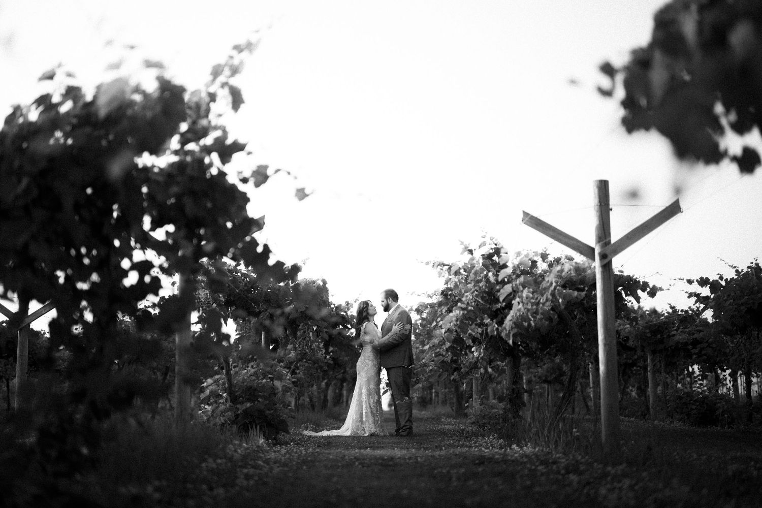 A black and white wedding photo with a rustic wooden cross in a garden setting.