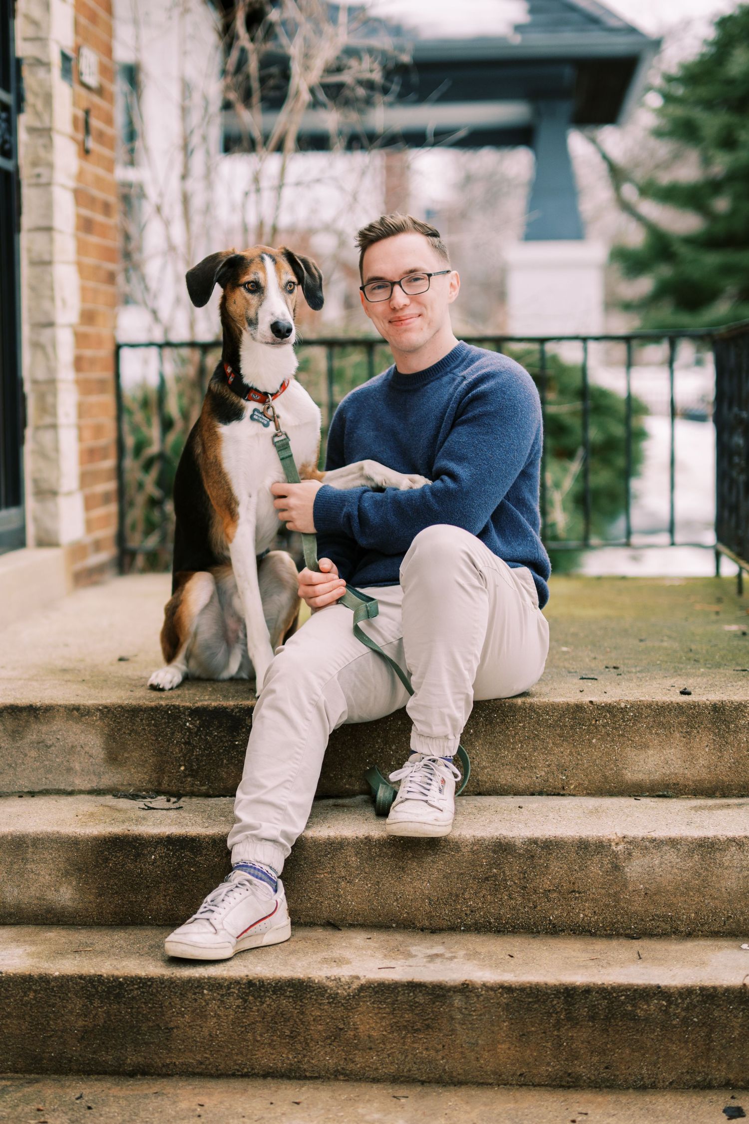 A brown and white dog sits with a companion on concrete steps outside a modern building.