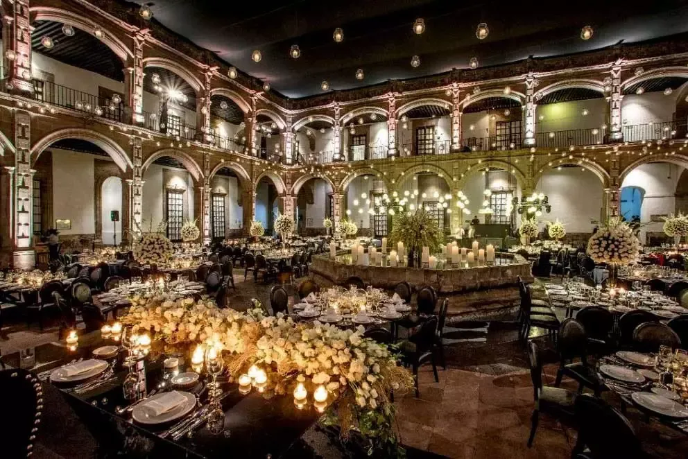Elegant wedding reception in historic venue with candlelit tables, lush floral arrangements, arched columns, and warm ambient lighting.