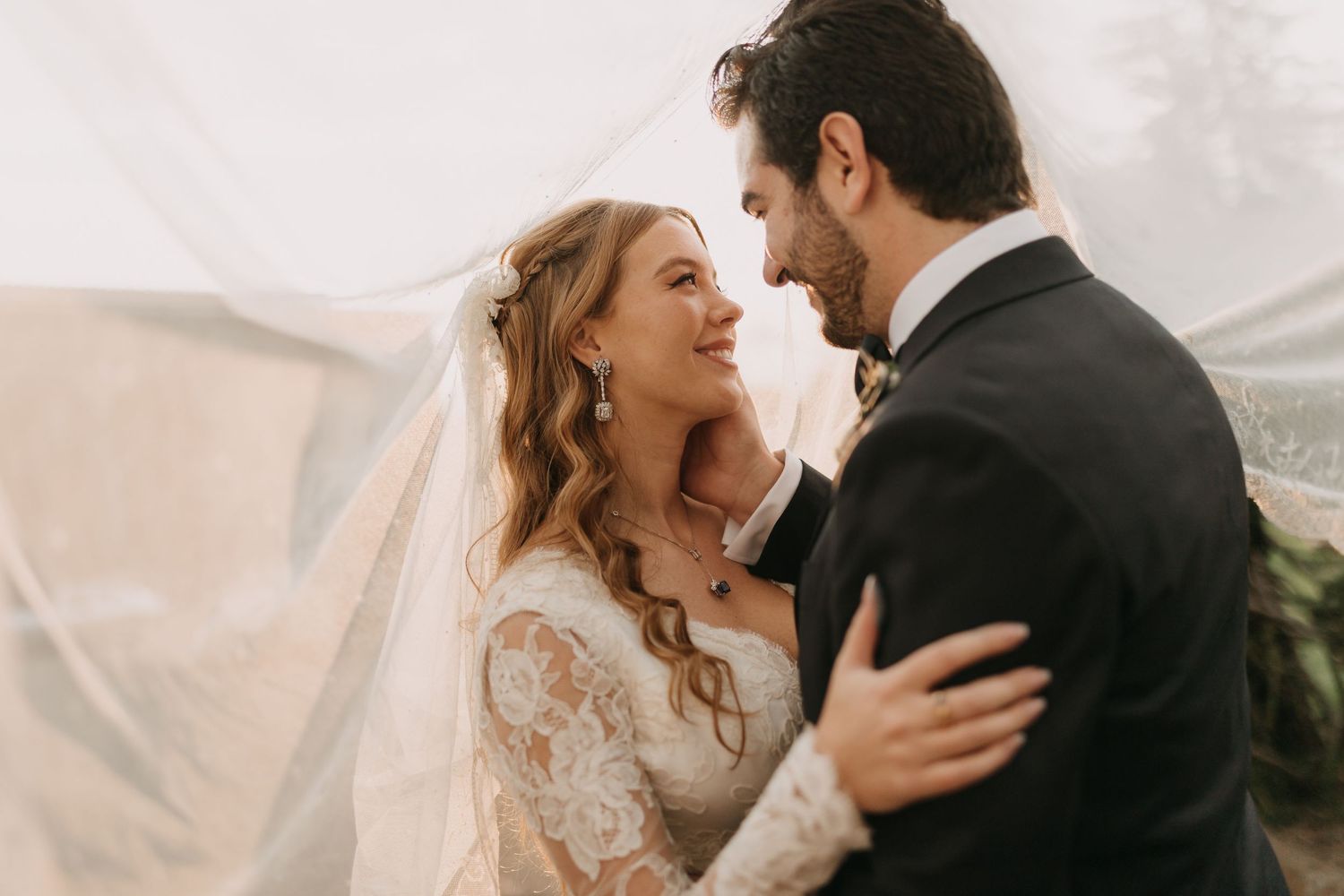 A bride and groom share a romantic moment under a flowing veil on their wedding day.