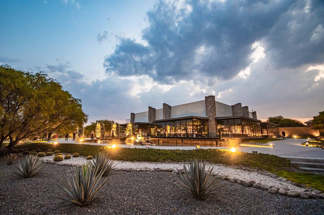 Modern desert resort building illuminated at dusk with agave plants, dramatic storm clouds, and warm pathway lighting.