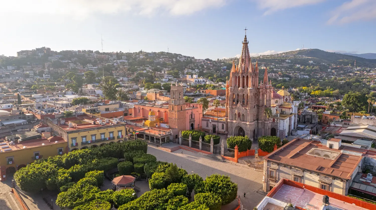 Aerial view of San Miguel de Allende with the iconic La Parroquia church and colorful cityscape under a blue sky.