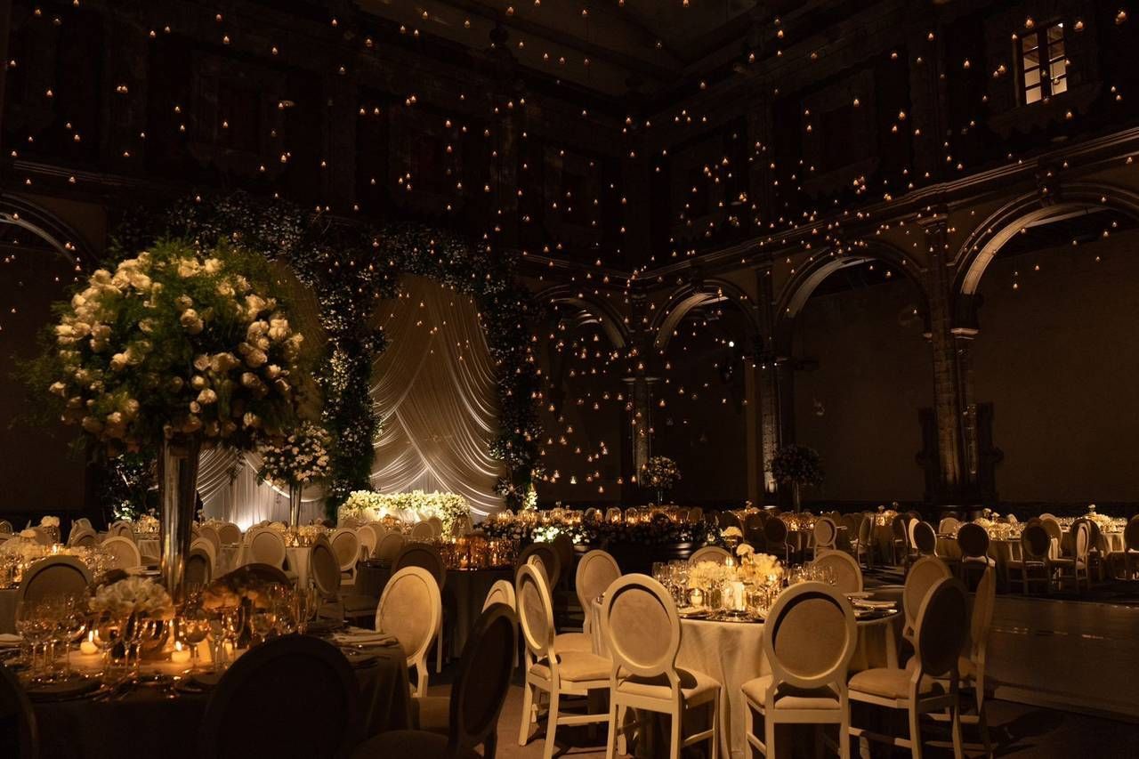 Elegant wedding reception with starlit ceiling, glowing floral centerpieces, and white chairs in a dark, romantic ballroom.