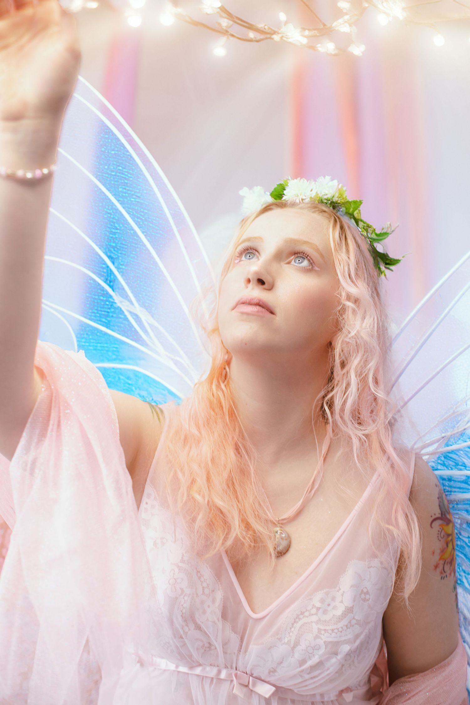 Ethereal fairy costume with glowing wings, flower crown, and pink tulle dress against soft pastel background.