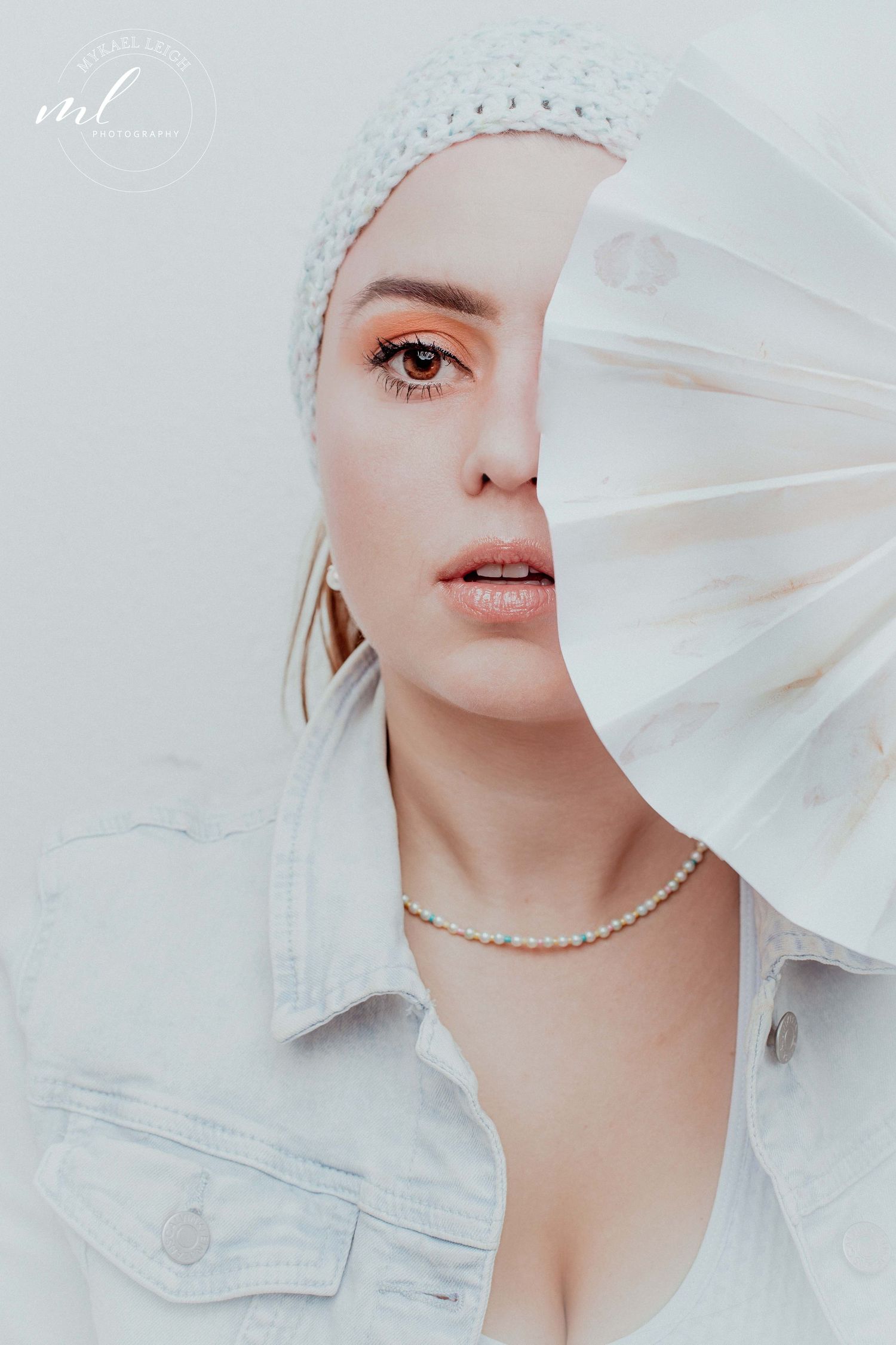 Ethereal portrait with white fabric veil and pearl necklace against light background featuring soft, delicate styling.