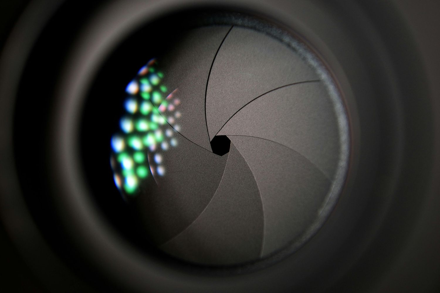 Close-up view of a camera lens aperture blades with a green light reflection showing the circular diaphragm pattern.