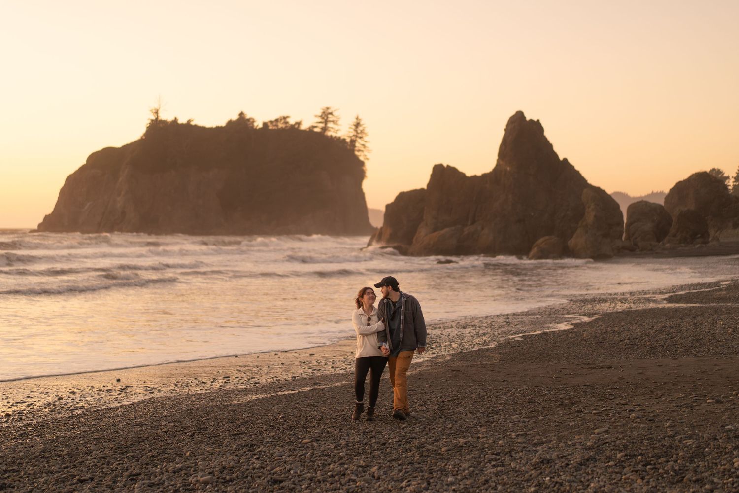 A couple embraces on Ruby beach at sunset with rocky cliffs and ocean waves in the background. captured by Savvy Photography - proposal