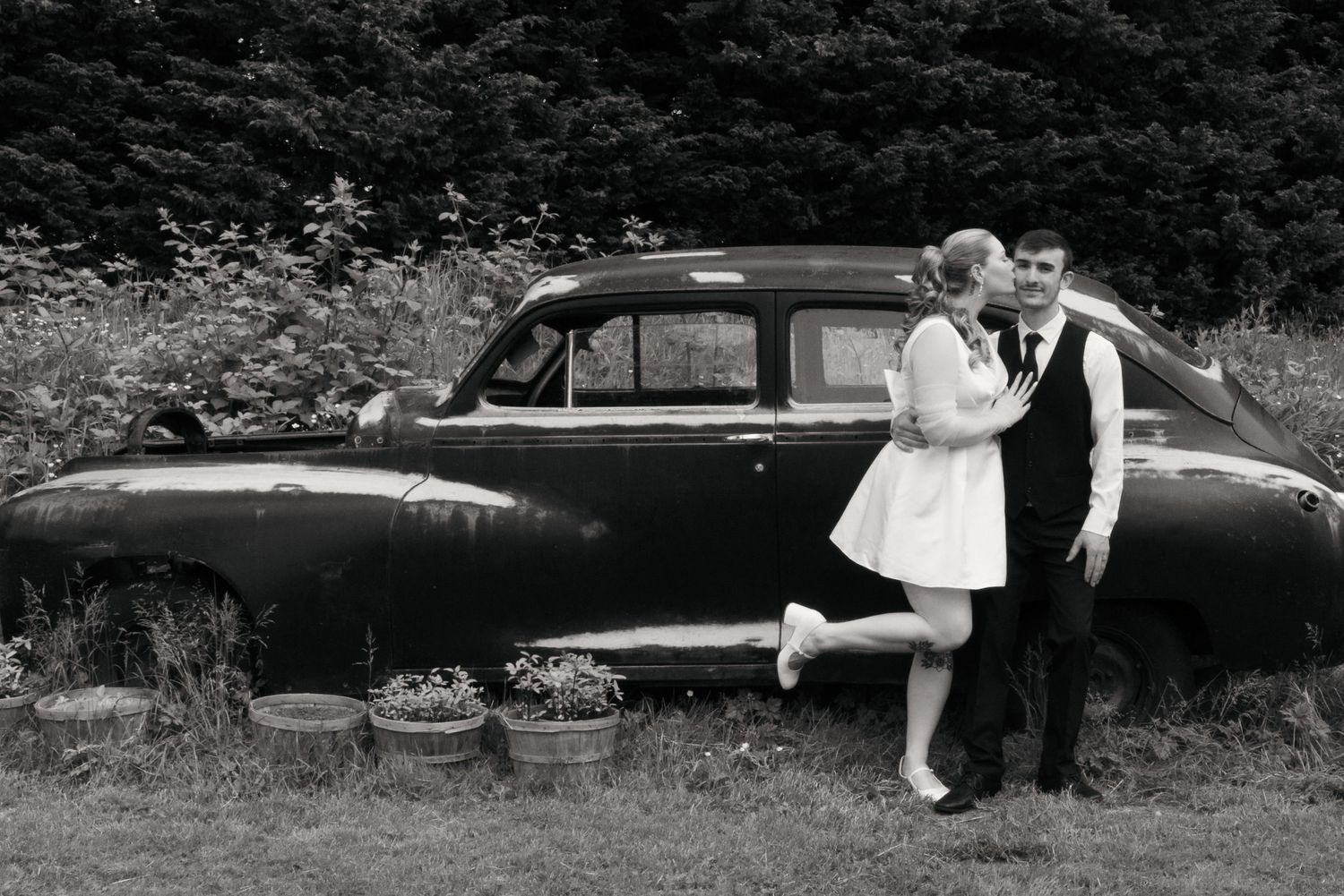 Vintage black and white photograph showing a series of people lounging on a park bench in casual summer attire.