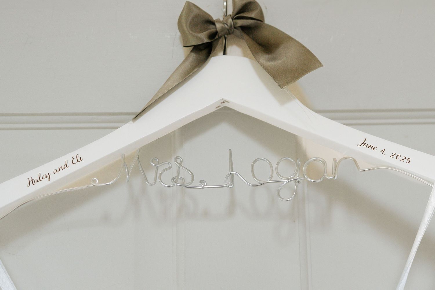 A white wooden wedding dress hanger with a taupe bow features personalized name lettering. captured by Savvy Photography - Seattle Wedding