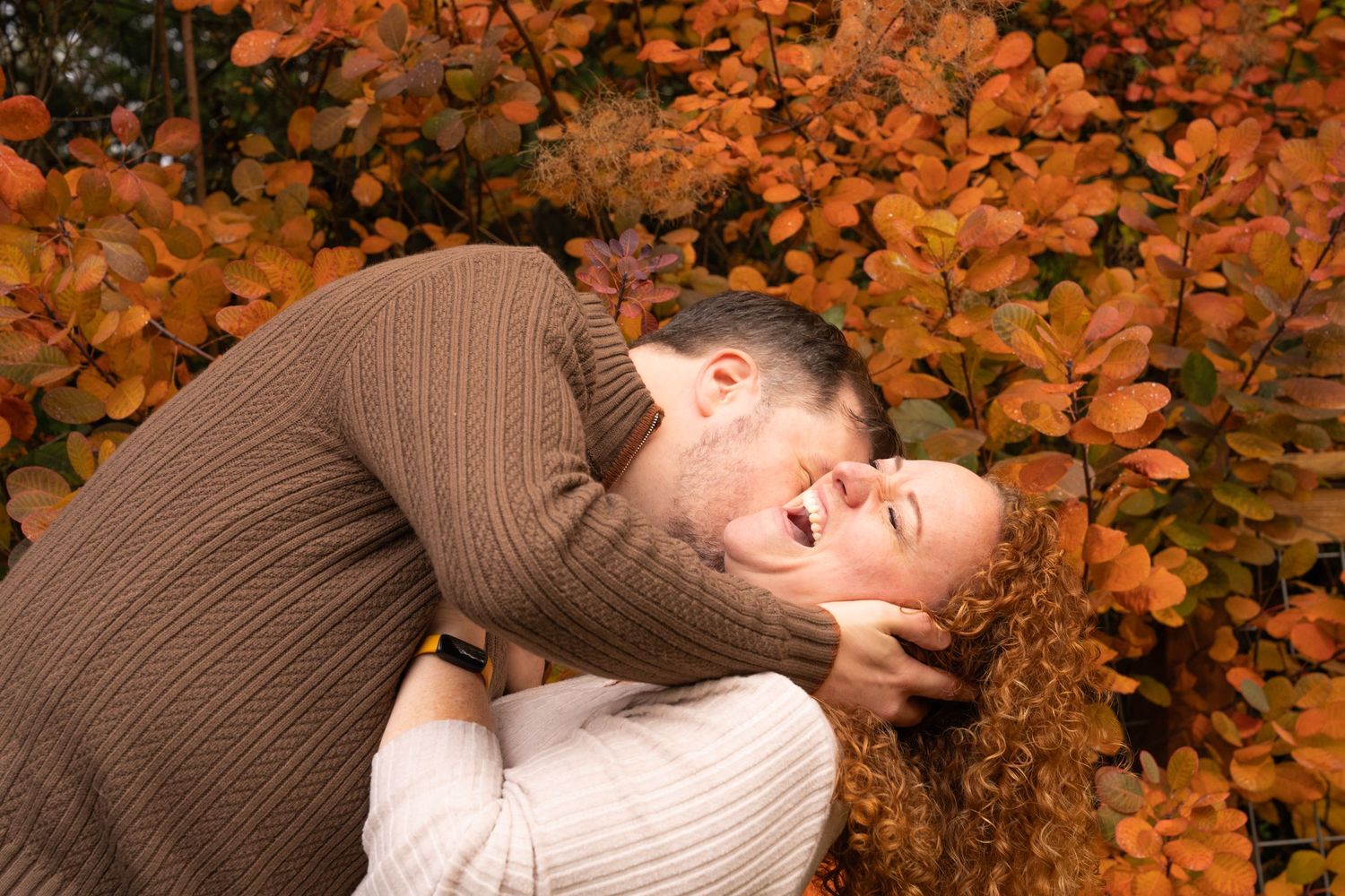 A couple shares a romantic kiss among vibrant orange autumn leaves in a park setting. captured by Savvy Photography - engagement photography